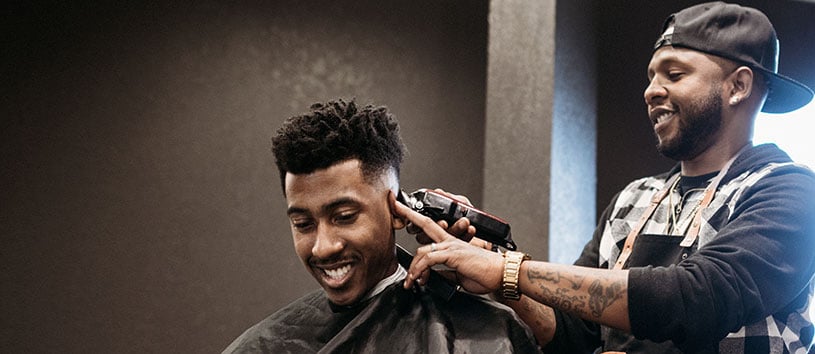 Barber client smiling while male barber finishes outlining the back of his head.